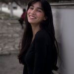 Portrait of a smiling young woman with long hair posing outdoors in casual attire.